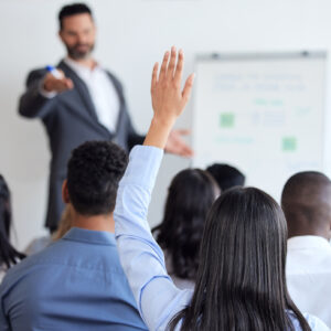 An apprentice raises their hand in a seminar to ask a question.