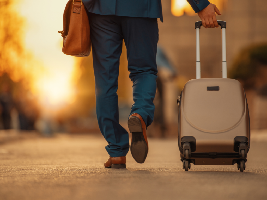 Man pulling a suitcase through the street in an autumn light.