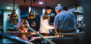 Moody photo of professional chefs working in a kitchen. Blue and copper tones.