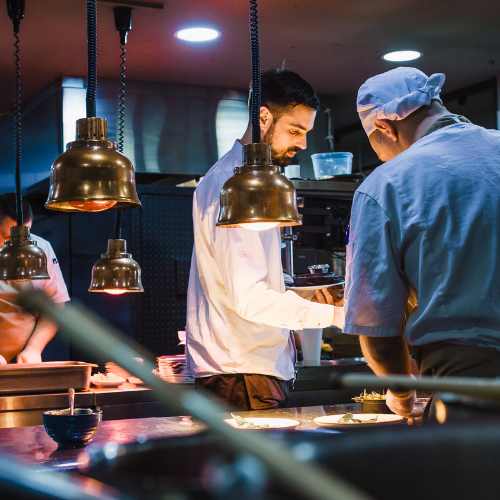 Moody photo of professional chefs working in a kitchen. Blue and copper tones.