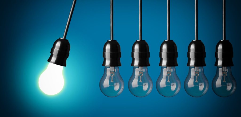 A chain of lightbulbs with one lit and swinging towards the others as if to create a chain reaction